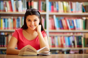 Portrait of cute girl with open book looking at camera in college library